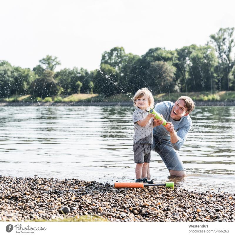 Father and son having fun at the riverside, playing with a water gun laughing Laughter riverbank Water gun father pa fathers daddy dads papa sons manchild