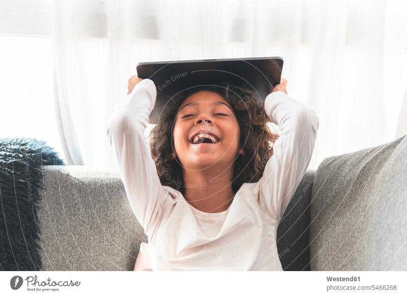 Portrait of little girl laughing on sofa with digital tablet in hands day daylight shot daylight shots day shots daytime portrait portraits testimonial portrait