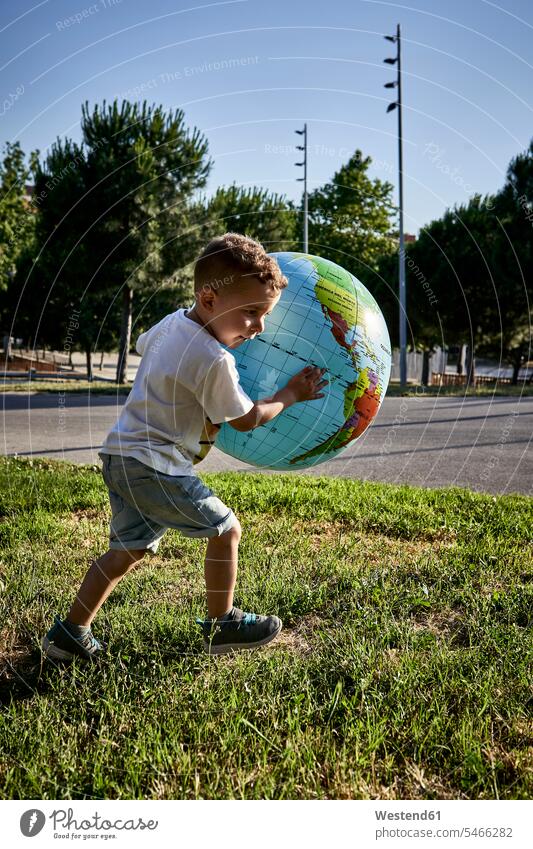 Carefree boy holding globe while running on grassy land during sunny day color image colour image Spain leisure activity leisure activities free time