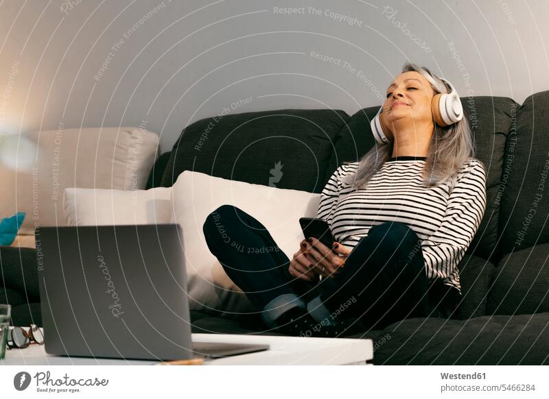 Smiling senior woman with mobile phone and laptop relaxing on sofa at home color image colour image indoors indoor shot indoor shots interior interior view