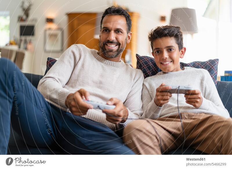 Happy father and son playing video game on couch in living room (value=0) human human being human beings humans person persons caucasian appearance