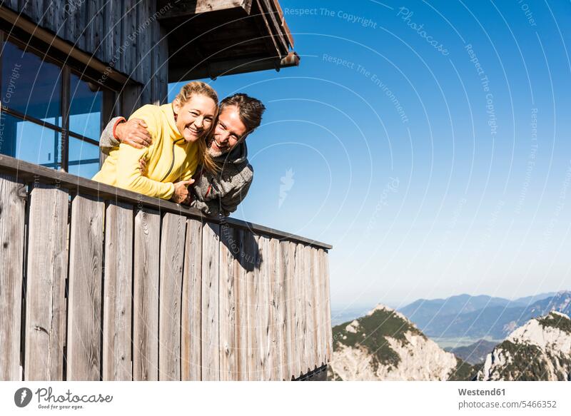 Couple leaning on balcony of a mountain hut, with arms around arm around mountain range mountains mountain ranges rested on balconies mountain pasture