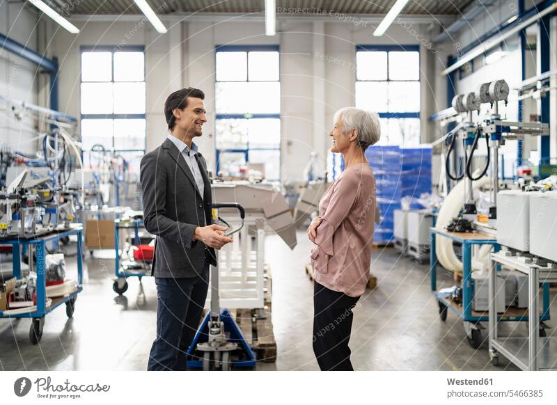 Smiling businessman and senior businesswoman talking in a factory speaking factories Businessman Business man Businessmen Business men businesswomen