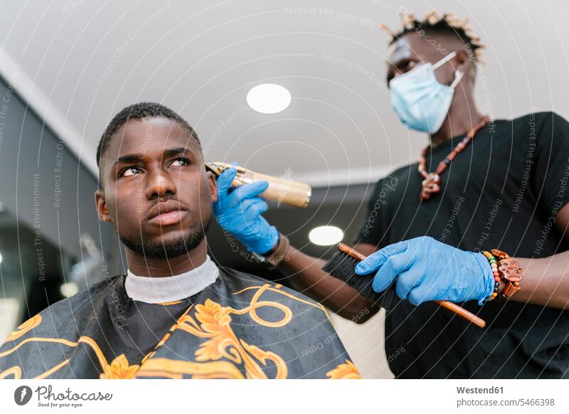Barber wearing mask and gloves while cutting customer's hair with razor in salon color image colour image Spain indoors indoor shot indoor shots interior