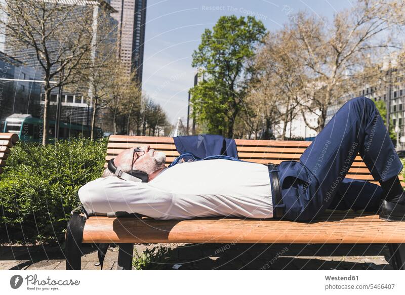 Mature businessman lying on a bench listening to music hearing laying down lie lying down benches Businessman Business man Businessmen Business men