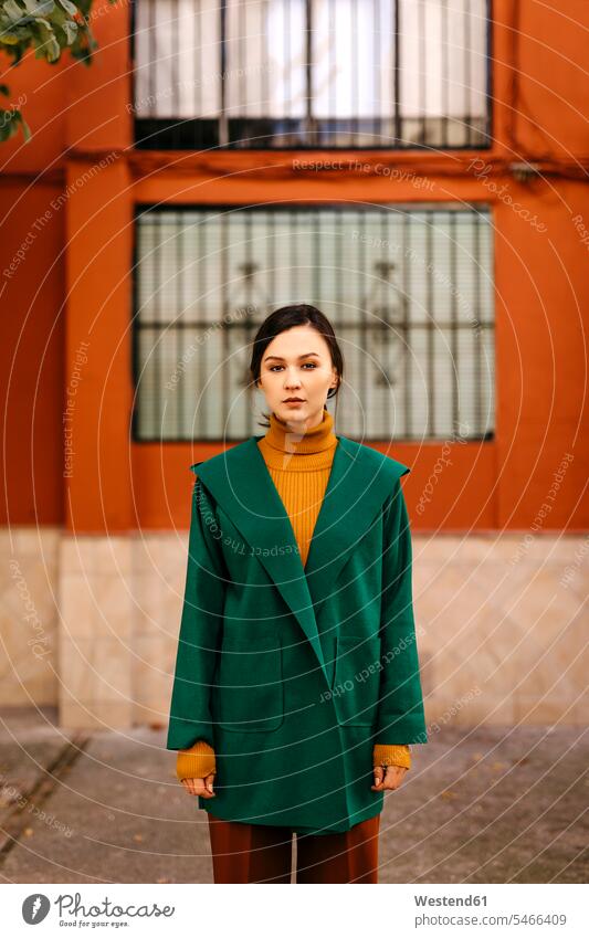 Young woman wearing green jacket standing against building in city color image colour image Spain casual clothing casual wear leisure wear casual clothes