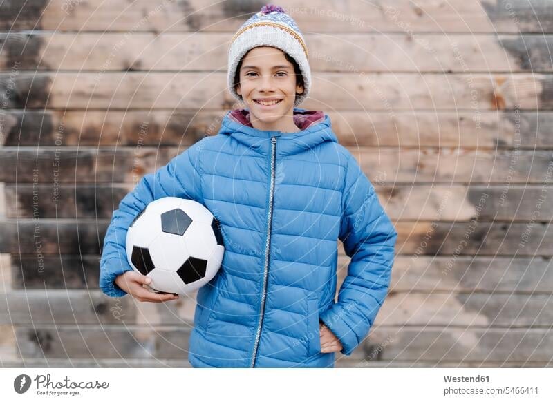 Smiling boy wearing warm clothing holding soccer ball while standing against wall color image colour image Spain leisure activity leisure activities free time