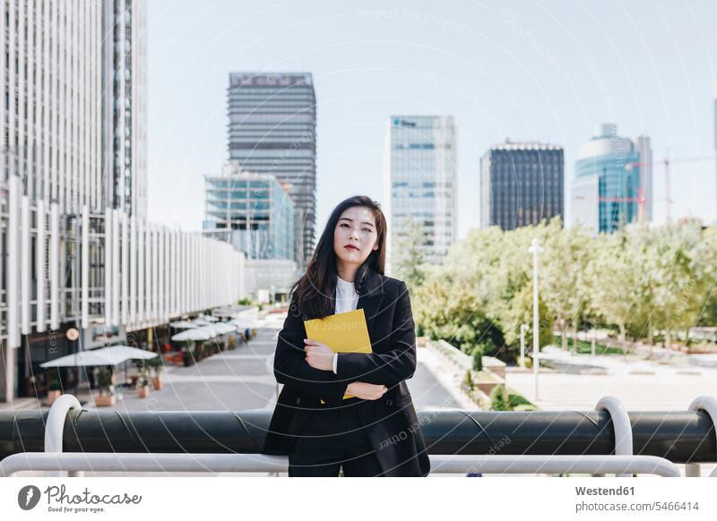 Confident businesswoman with book standing against downtown district in city color image colour image outdoors location shots outdoor shot outdoor shots day