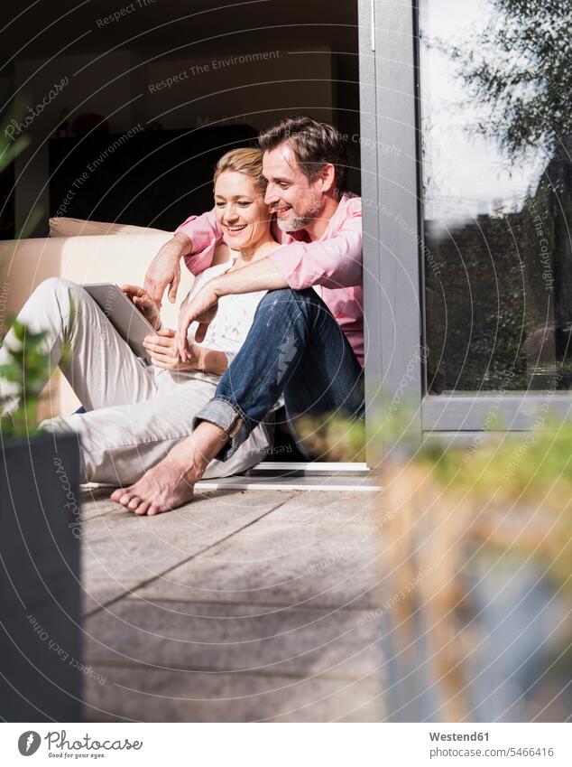Mature couple relaxing together at open terrace door using tablet relaxation patio door French window twosomes partnership couples use people persons