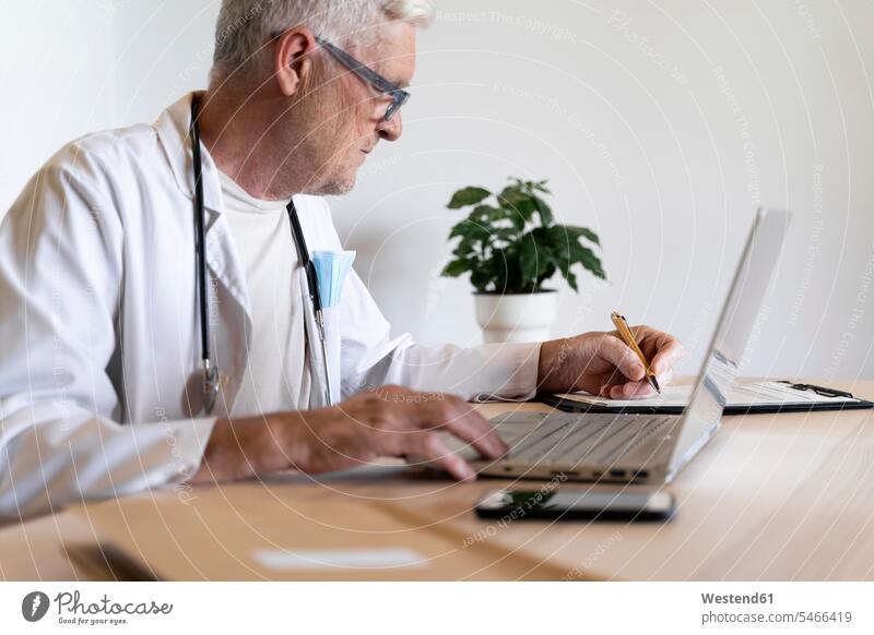 Senior doctor working on laptop while sitting in his clinic color image colour image indoors indoor shot indoor shots interior interior view Interiors day