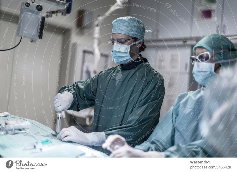 Neuroradiologist with assistant using syringe during an operation surgery surgeries operating surgical gown scrubs Operating Gown hospital Medical Clinic doctor