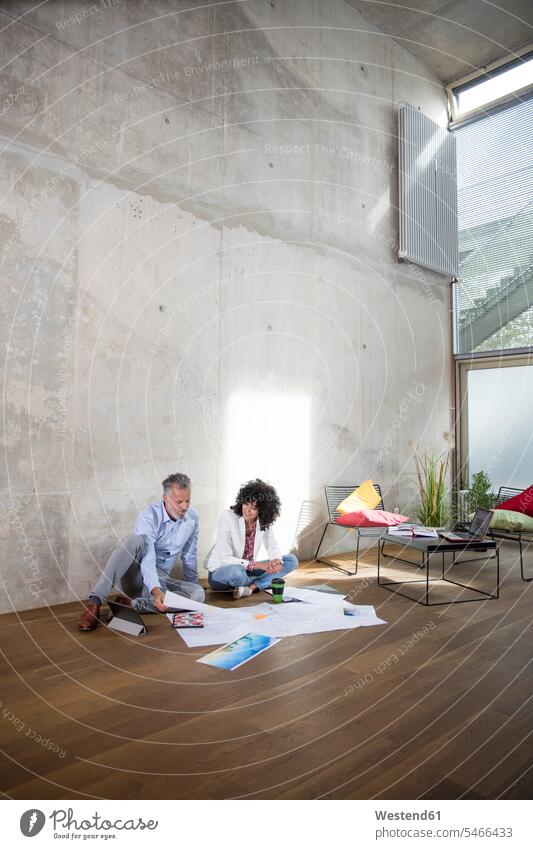 Businessman and businesswoman sitting on the floor in a loft discussing documents Business man Businessmen Business men Seated businesswomen business woman