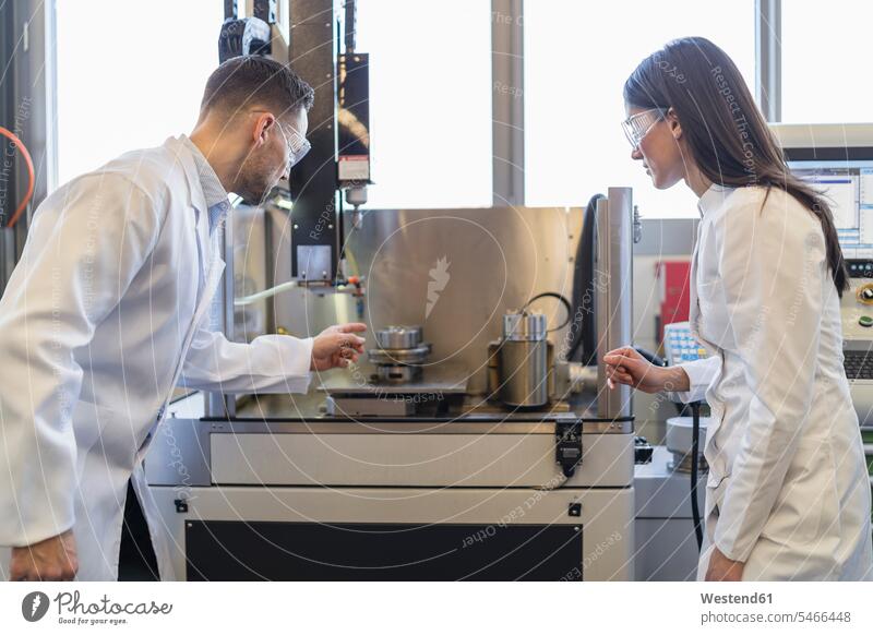 Colleagues wearing lab coats and safety goggles looking at machine in modern factory colleagues factories contemporary Laboratory Coat Labcoats Lab Coat