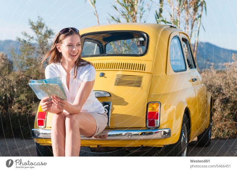Portrait of laughing woman with map sitting on bumper of yellow vinage car, Sardinia, Italy maps motor vehicles road vehicle road vehicles Auto automobile