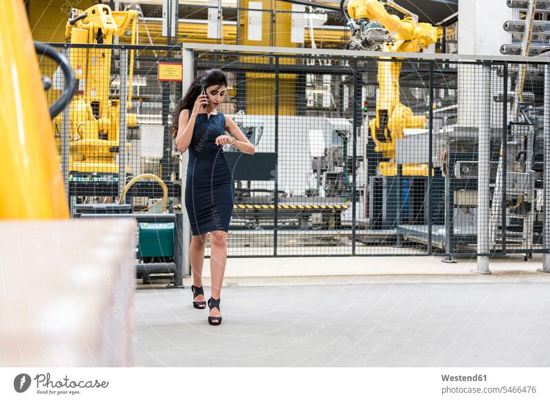 Woman on the phone walking in factory shop floor with industrial robot checking the time woman females women factories industrial hall factory hall