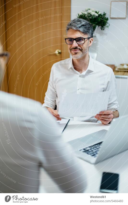 Smiling man at desk holding paper looking at colleague colleagues men males eyeing smiling smile home at home Businessman Business man Businessmen Business men