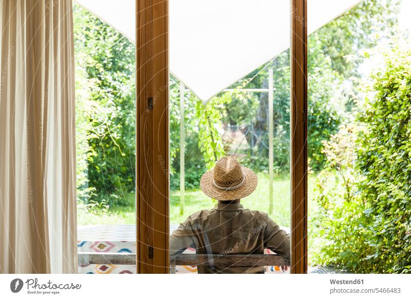 Back view of senior man wearing straw hat on terrace enjoying his garden Germany sunset years evening of life getting away from it all Getting Away From All