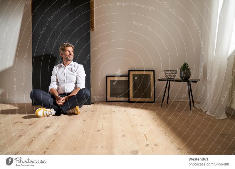 Portrait of relaxed mature man sitting on the floor at home looking at distance frame frames picture frames shirts colour colours White Colors free time