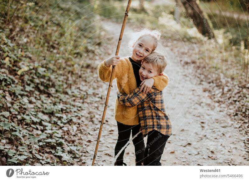 Sister holding stick while embracing brother standing in forest color image colour image outdoors location shots outdoor shot outdoor shots 4-5 years