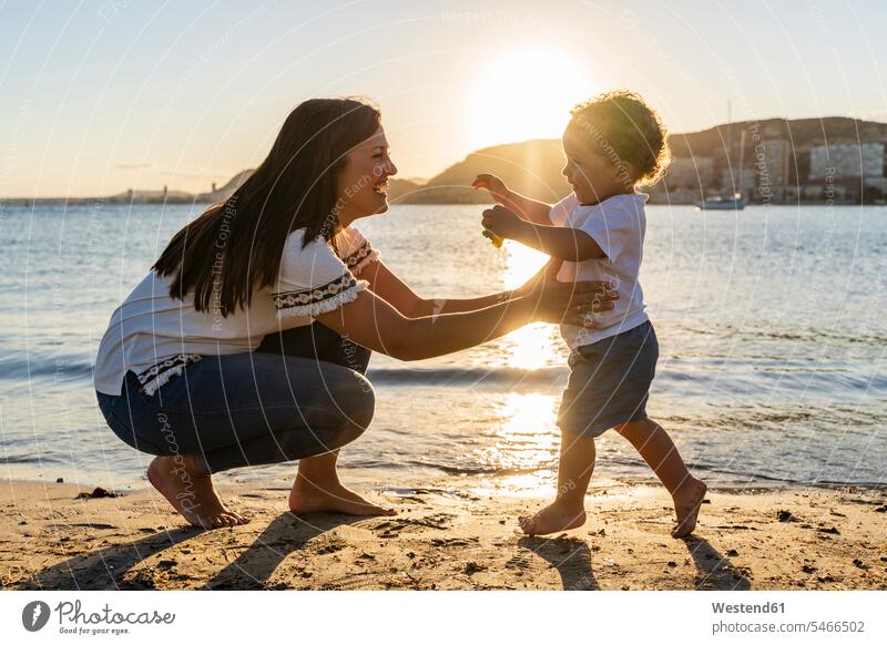 Cheerful mother playing with son at beach during sunset color image colour image Spain leisure activity leisure activities free time leisure time