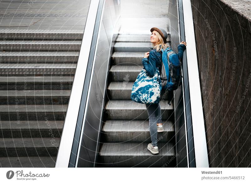 Woman with backpack and travelling bag standing on escalator looking up caucasian caucasian ethnicity caucasian appearance european indoors indoor shot