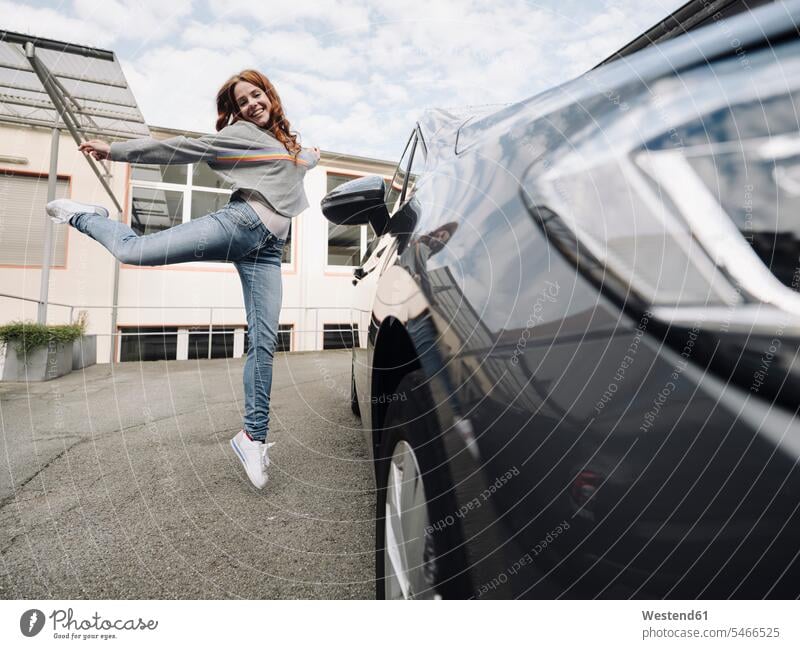Happy redheaded woman jumping beside car motor vehicles road vehicle road vehicles Auto automobile Automobiles cars motorcar motorcars smile Ardor Ardour
