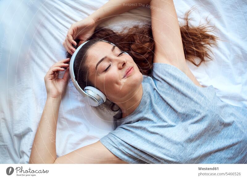Portrait of happy young woman with eyes closed lying on bed listening music with headphones human human being human beings humans person persons