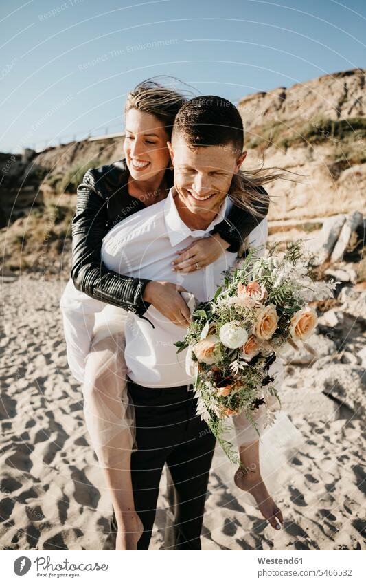 Happy groom carrying bride piggyback on the beach Celebration Event Celebrations Ceremonies Ceremony Festivities Festivity getting married Marriage marrying