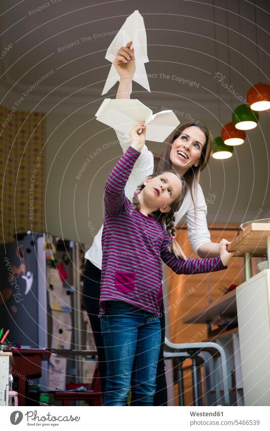 Happy mother and daughter throwing paper plane together at home mommy mothers ma mummy mama paper dart paper planes paper darts paper aeroplane Paper Airplane