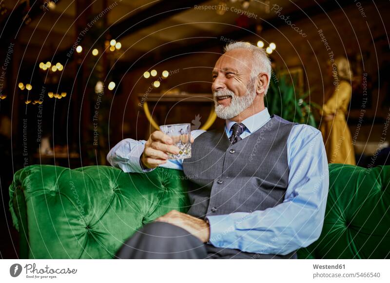 Portrait of elegant senior man sitting on couch in a bar holding tumbler portrait portraits settee sofa sofas couches settees men males chic elegance stylishly