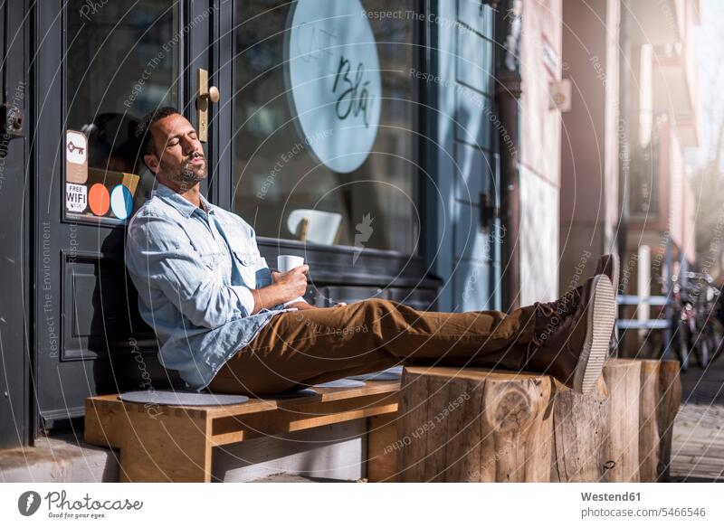 Relaxed man sitting outside a cafe enjoying the sunshine indulgence enjoyment savoring indulging Seated males Sunny Day sunny relaxed relaxation pleasure Adults