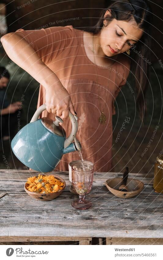 Beautiful woman pouring hot water in glass while preparing herbal tea on wooden table color image colour image indoors indoor shot indoor shots interior