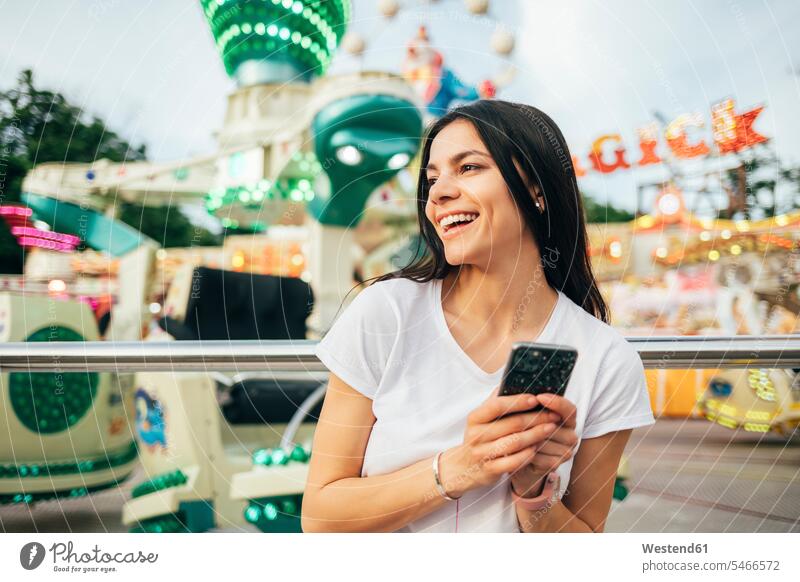 Cheerful young woman holding smart phone looking away at amusement park color image colour image Ukraine leisure activity leisure activities free time