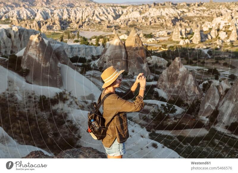 Side view of young woman photographing rock formations with smart phone in Goreme, Cappadocia, Turkey Adventure Adventures adventurous backpack rucksack