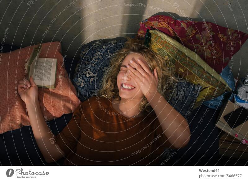 Portrait of laughing young woman lying on bed reading a book human human being human beings humans person persons caucasian appearance caucasian ethnicity