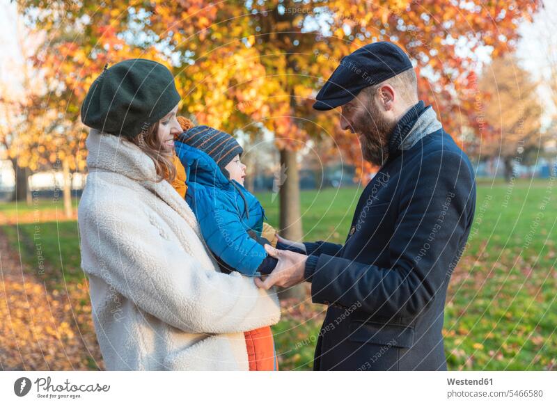 Happy affectionate couple with baby son at park coat coats jackets caps hat hats hold smile play delight enjoyment Pleasant pleasure Cheerfulness exhilaration