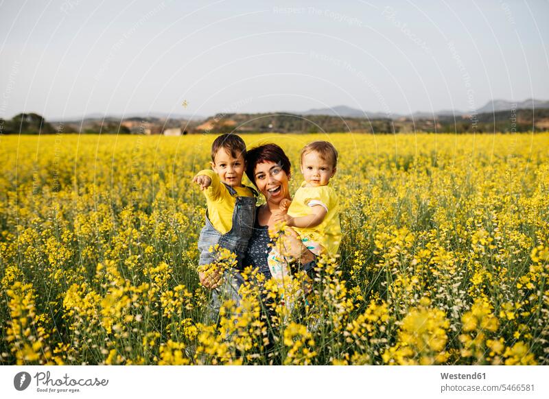 Spain, portrait of laughing mother with little son and daughter in a rape field portraits sons manchild manchildren daughters mommy mothers mummy mama Laughter