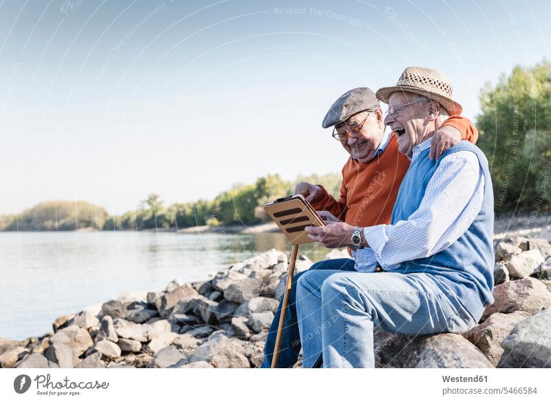 Two old friends sitting by the riverside, using digital tablet Seated use riverbank Best Friend Best Friends Best Pal digitizer Tablet Computer Tablet PC