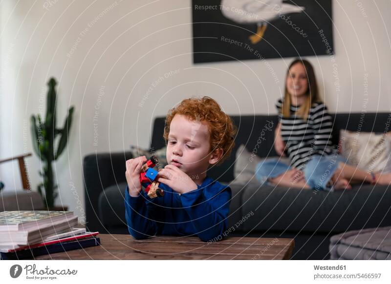Mother relaxing on sofa while son playing with toy robot on table at home color image colour image leisure activity leisure activities free time leisure time