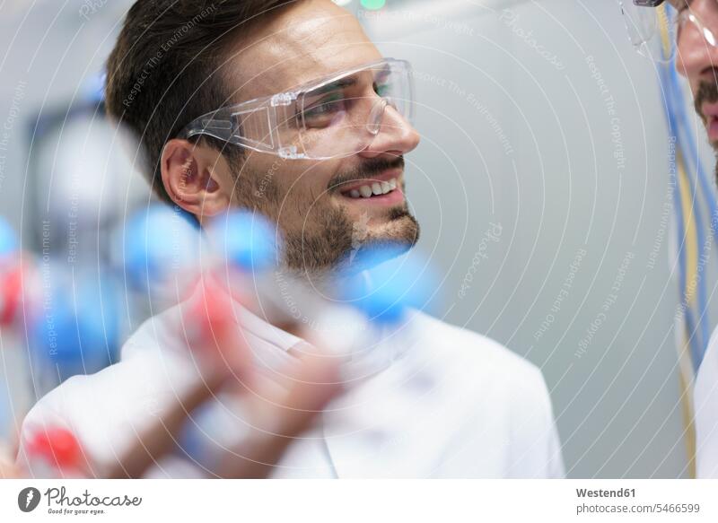 Smiling male scientist holding molecular structure while looking at colleague in illuminated laboratory color image colour image indoors indoor shot