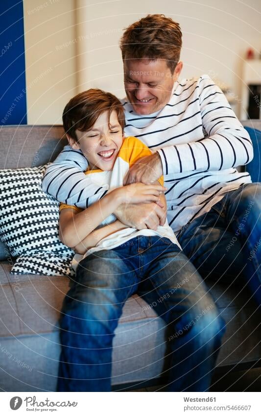 Carefree father and son having fun on couch at home settee sofa sofas couches settees Fun funny carefree pa fathers daddy dads papa sons manchild manchildren