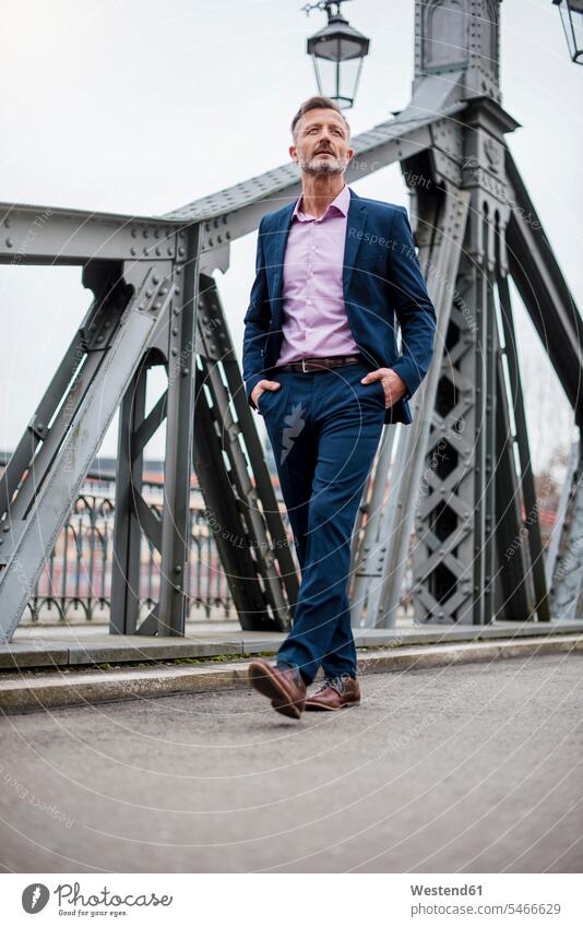 Stylish mature businessman wearing blue suit walking on bridge Fullsuit suits full suit bridges going style stylish portrait portraits Businessman Business man