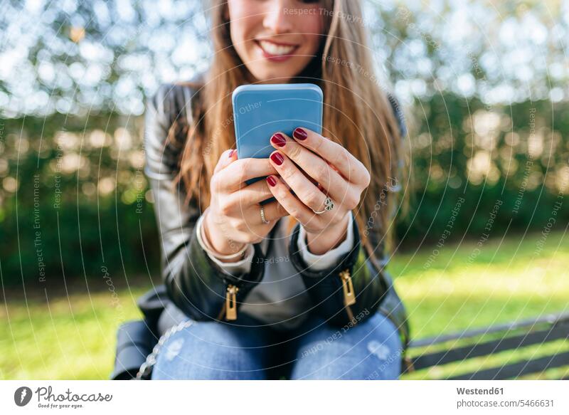 Close-up of young woman sitting on a bench in park using cell phone Seated parks benches mobile phone mobiles mobile phones Cellphone cell phones females women