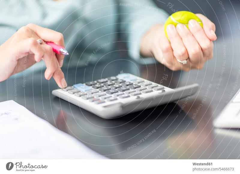 Woman at desk in office using calculator and stress ball woman females women businesswoman businesswomen business woman business women desks stress balls