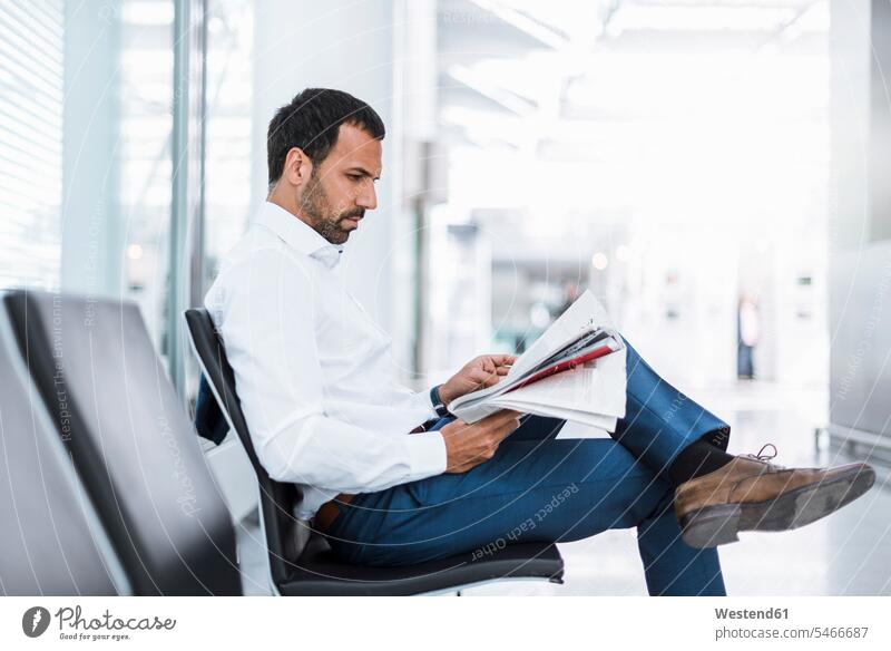 Businessman reading a newspaper in waiting hall Business man Businessmen Business men portrait portraits males sitting Seated newspapers business people