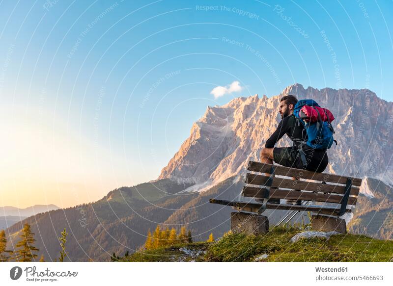 Austria, Tyrol, Hiker taking a break, sitting on bench, looking at view Taking a Break resting wooden bench hiker wanderers hikers sunset sunsets sundown