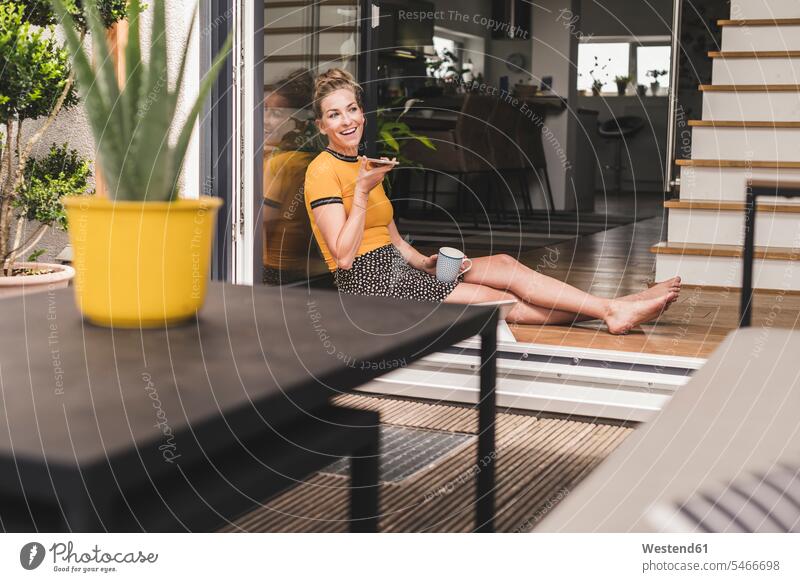 Relaxed woman sitting at terrace door at home using smartphone human human being human beings humans person persons celibate celibates singles solitary people