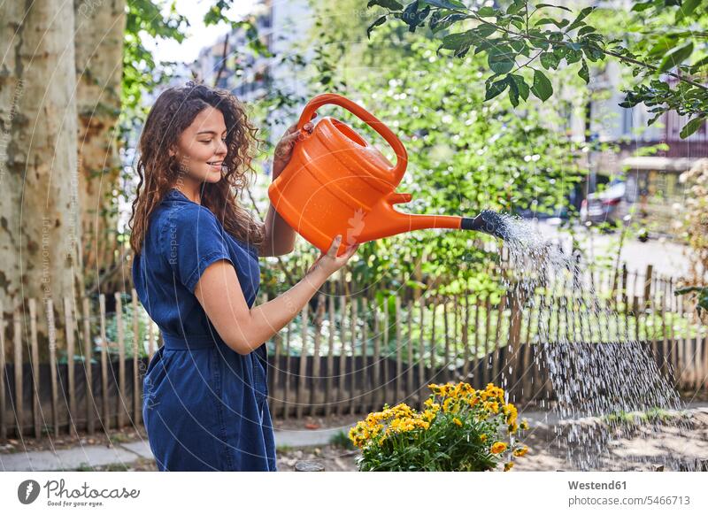 Young woman watering flowers in garden fences hold seasons summer time summertime summery delight enjoyment Pleasant pleasure happy content Contented Emotion