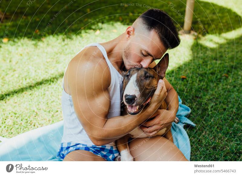Muscular man sitting on blanket on a meadow hugging his dog animals creature creatures domestic animal pet Canine dogs Blankets relax relaxing Seated embrace
