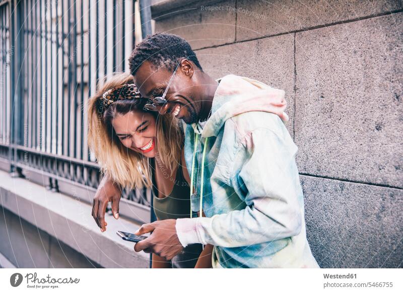 Laughing couple using cell phone outdoors human human being human beings humans person persons African black black ethnicity coloured caucasian appearance